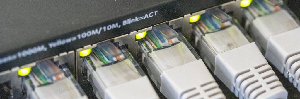 A photo of Cat5e Ethernet cables plugged into a switch, link lights on the ethernet ports are illuminated.